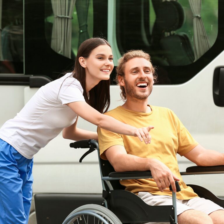 Support worker and smiling young man in a wheelchair beside an accessible van