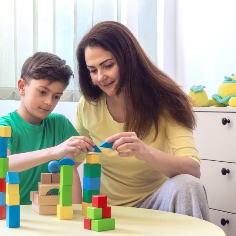 Support worker and young boy building with colourful wooden blocks