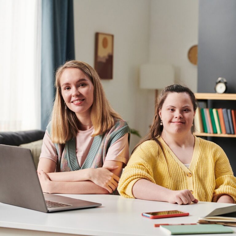 Smiling support worker and young woman sitting together at a table at home
